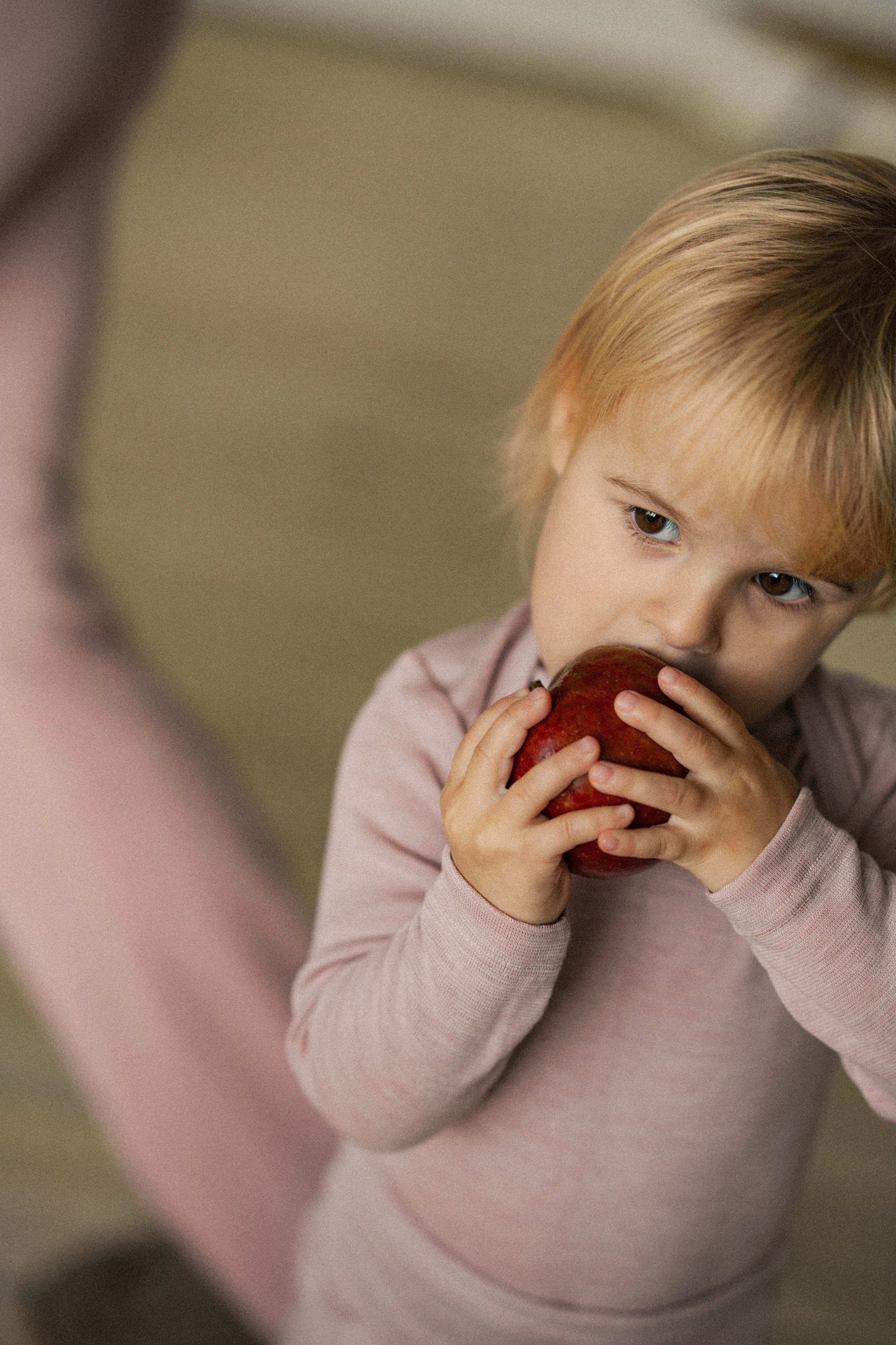 Toddler wearing wool-silk essentials jersey set (body and leggins) in rose color, eating an apple